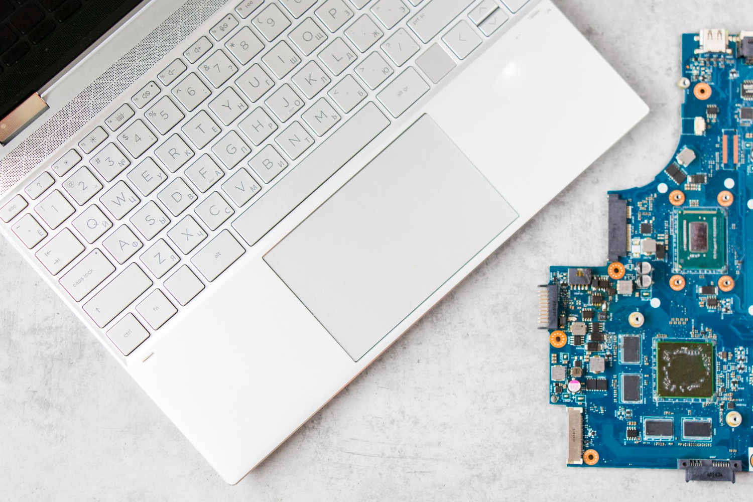Laptop keyboard next to its circuit board on gray surface
