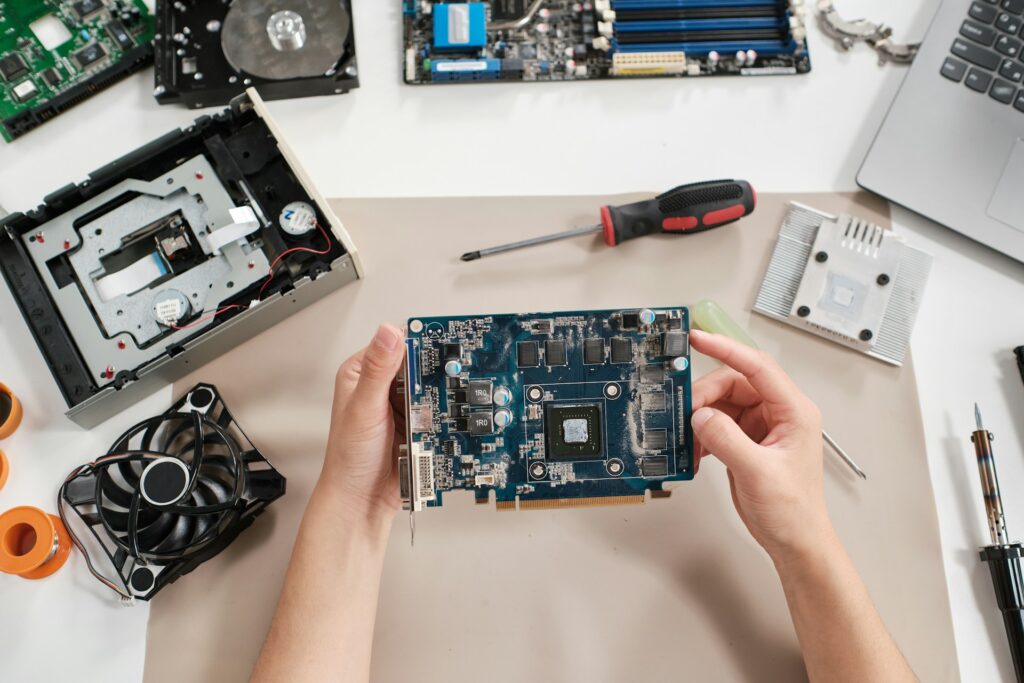 Data Recovery - Hands holding computer graphics card with repair tools and laptop parts
